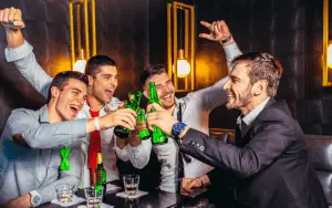 Eine lebhafte Gruppe von Freunden, lachend und unterhaltsam, während sie auf einer aufregenden Pub Crawl Tour durch die belebten Straßen einer Stadt unterwegs sind. Die Gruppe ist in verschiedenen Bars und Pubs und Clubs zu sehen, wo sie in fröhlicher Stimmung verschiedene Getränke probieren und die einzigartige Atmosphäre jeder Location genießen. Die bunten Lichter der Bars leuchten in der Nacht, und die Teilnehmer tauschen fröhliche Gespräche und Toasts aus, während sie die lokale Bar-Szene erkunden. Ein unvergessliches Abenteuer, das Freundschaften schmiedet und die Nacht in lebendige Erinnerungen verwandelt. Junggesellenabschied | JGA