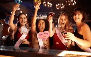 Eine lebhafte Gruppe von Freunden, lachend und unterhaltsam, während sie auf einer aufregenden Pub Crawl Tour durch die belebten Straßen einer Stadt unterwegs sind. Die Gruppe ist in verschiedenen Bars und Pubs und Clubs zu sehen, wo sie in fröhlicher Stimmung verschiedene Getränke probieren und die einzigartige Atmosphäre jeder Location genießen. Die bunten Lichter der Bars leuchten in der Nacht, und die Teilnehmer tauschen fröhliche Gespräche und Toasts aus, während sie die lokale Bar-Szene erkunden. Ein unvergessliches Abenteuer, das Freundschaften schmiedet und die Nacht in lebendige Erinnerungen verwandelt. JGA | Junggesellinnenabschied