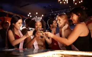 Eine lebhafte Gruppe von Freunden, lachend und unterhaltsam, während sie auf einer aufregenden Pub Crawl Tour durch die belebten Straßen einer Stadt unterwegs sind. Die Gruppe ist in verschiedenen Bars und Pubs und Clubs zu sehen, wo sie in fröhlicher Stimmung verschiedene Getränke probieren und die einzigartige Atmosphäre jeder Location genießen. Die bunten Lichter der Bars leuchten in der Nacht, und die Teilnehmer tauschen fröhliche Gespräche und Toasts aus, während sie die lokale Bar-Szene erkunden. Ein unvergessliches Abenteuer, das Freundschaften schmiedet und die Nacht in lebendige Erinnerungen verwandelt. JGA | Junggesellinnenabschied