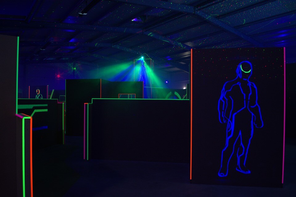 die Kulisse der LaserTag-Arena im Dunklen und mit Hindernissen, die durch Neon-Beleuchtung beleuchtet werden
