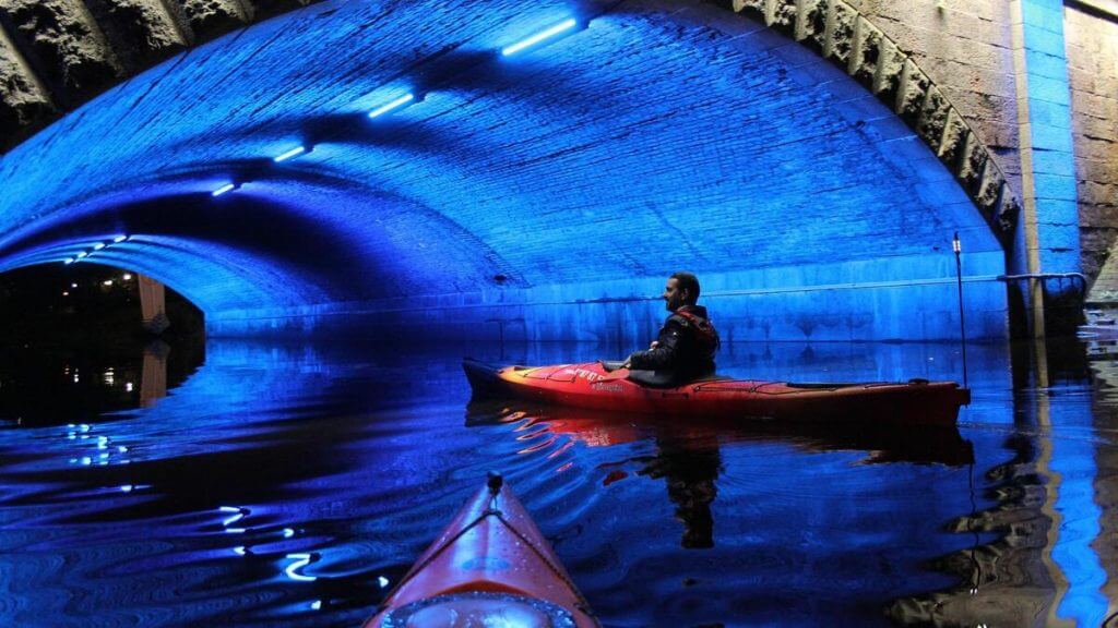 ein Kanufahrer fährt unter einer blau beleuchteten Brücke in Leipzig durch