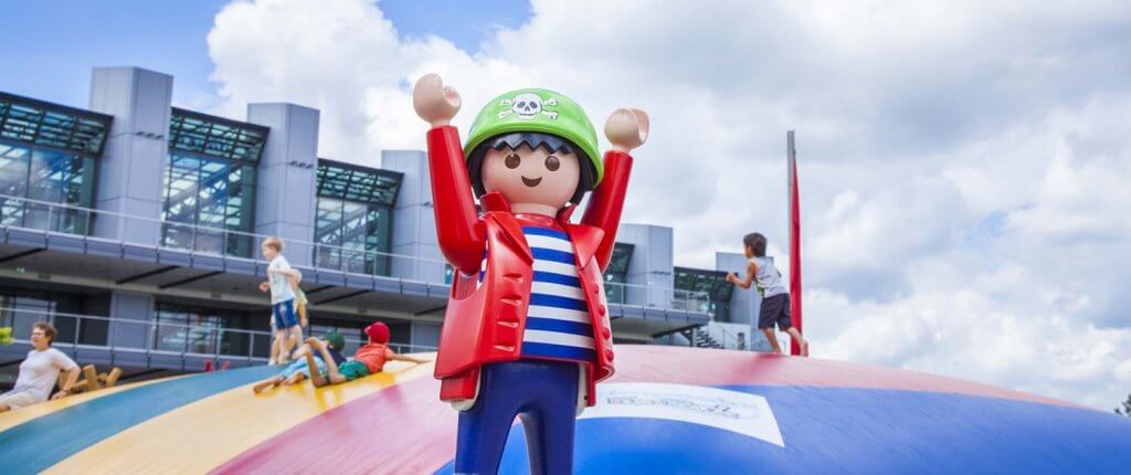 eine große Playmobil-Figur steht vor einem großen Sprungkissen für Kinder im Playmobil-Land