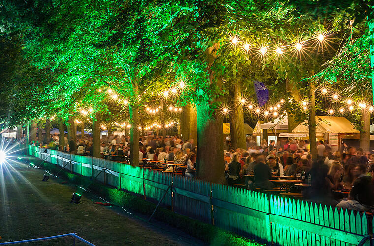 Nachtaufnahme eines Weihnfestes mit Bierbänken unter Bäumen und Lichterketten