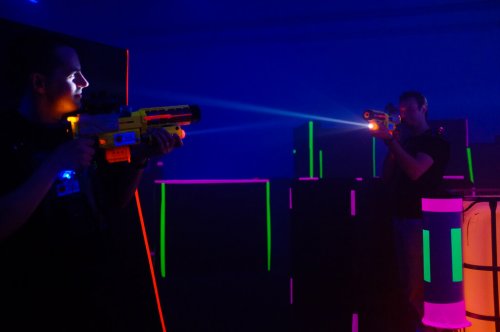 zwei Personen spielen Lasertag zwischen neon-beleuchteten Hindernissen