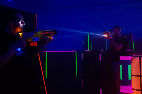 zwei Personen spielen Lasertag zwischen neon-beleuchteten Hindernissen
