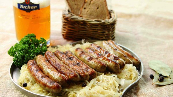 Teller in Herzform mit Sauerkraut und Nürnberger Bratwürsten, einem Glas Bier und einem Brotkorb